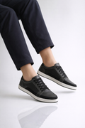 Black sneakers worn with navy pants on a white background