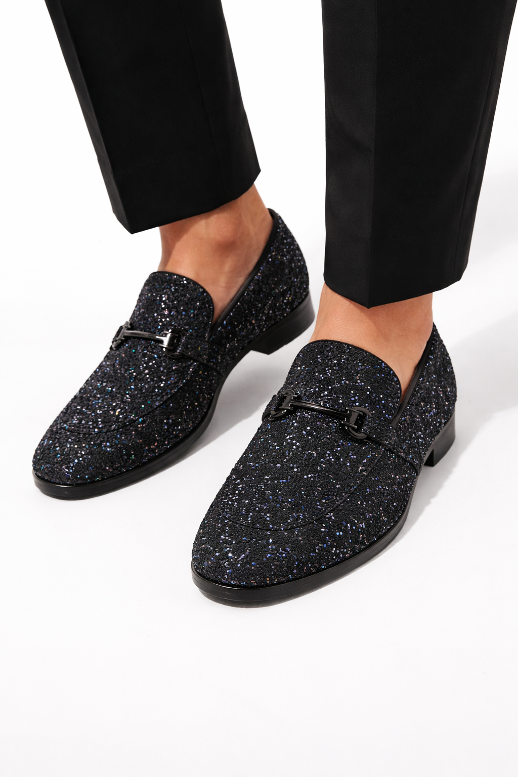 Black glittery loafers worn with black pants on a white background